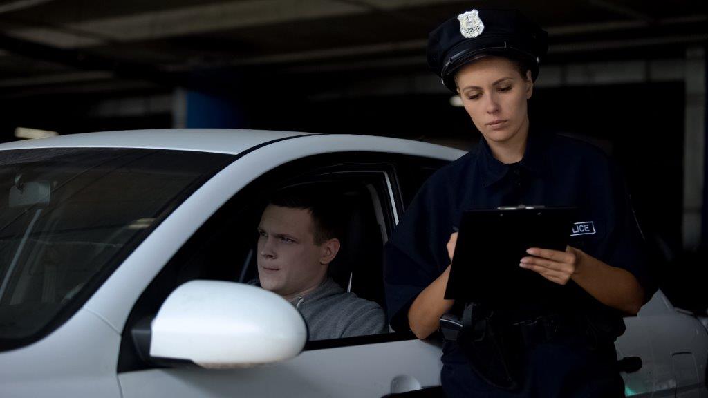 female officer writing on a clipboard next to a man in a white car